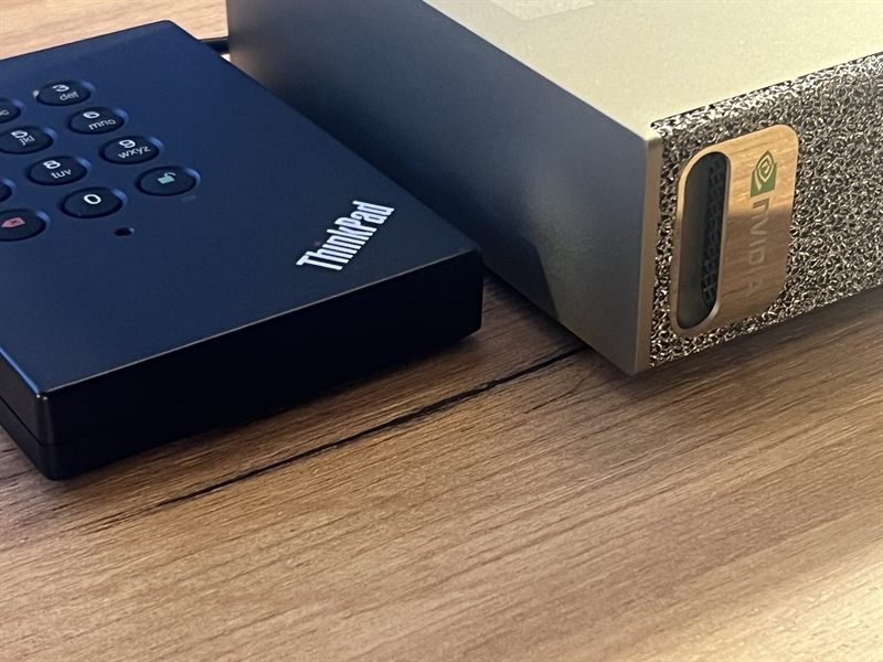 Compact gold-cased AI workstation on a wooden desk, next to an encrypted external hard drive with a PIN keypad
